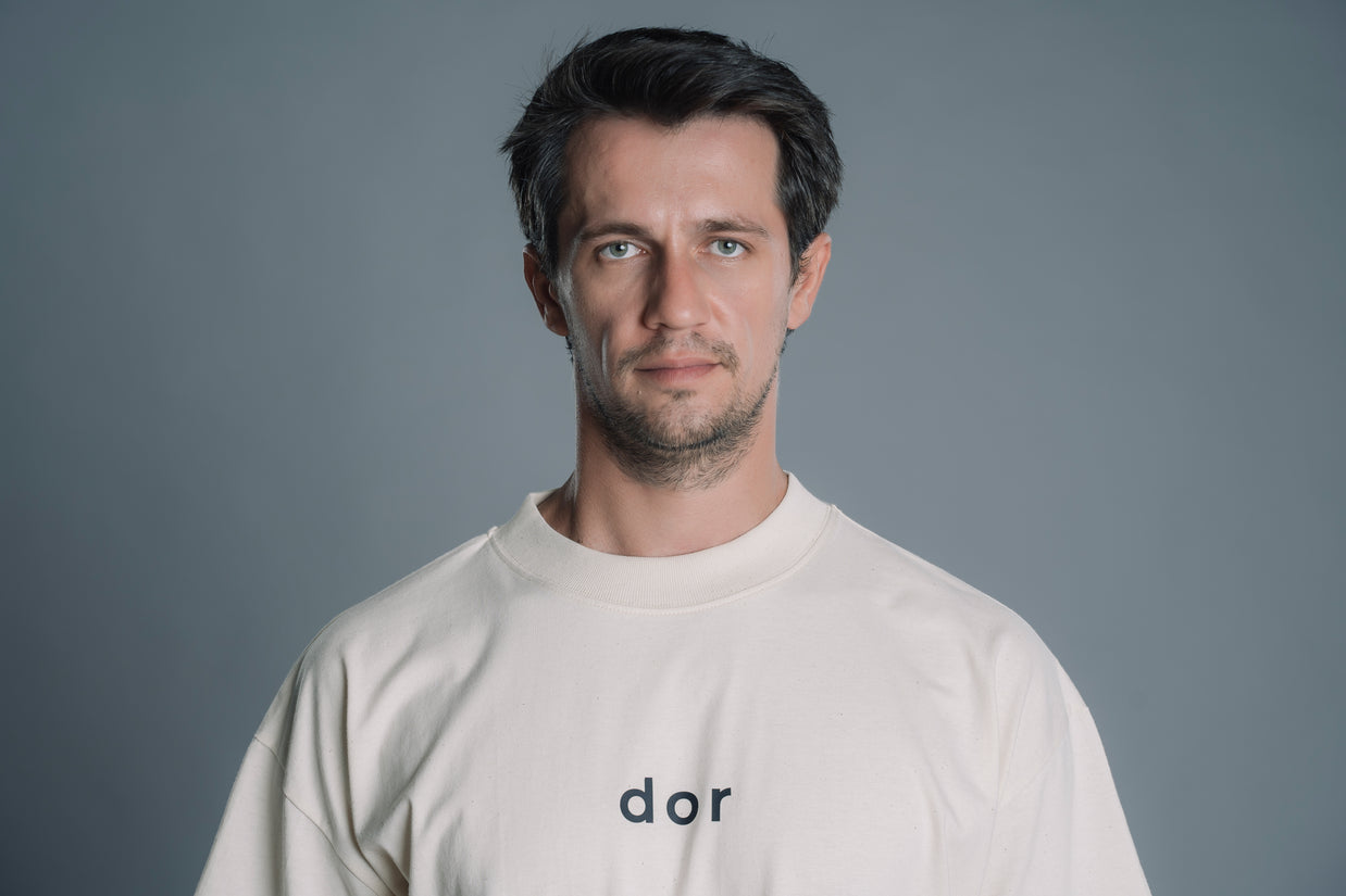 Man wearing a Natural RAW tshirt with 'dor' logo against a gray background