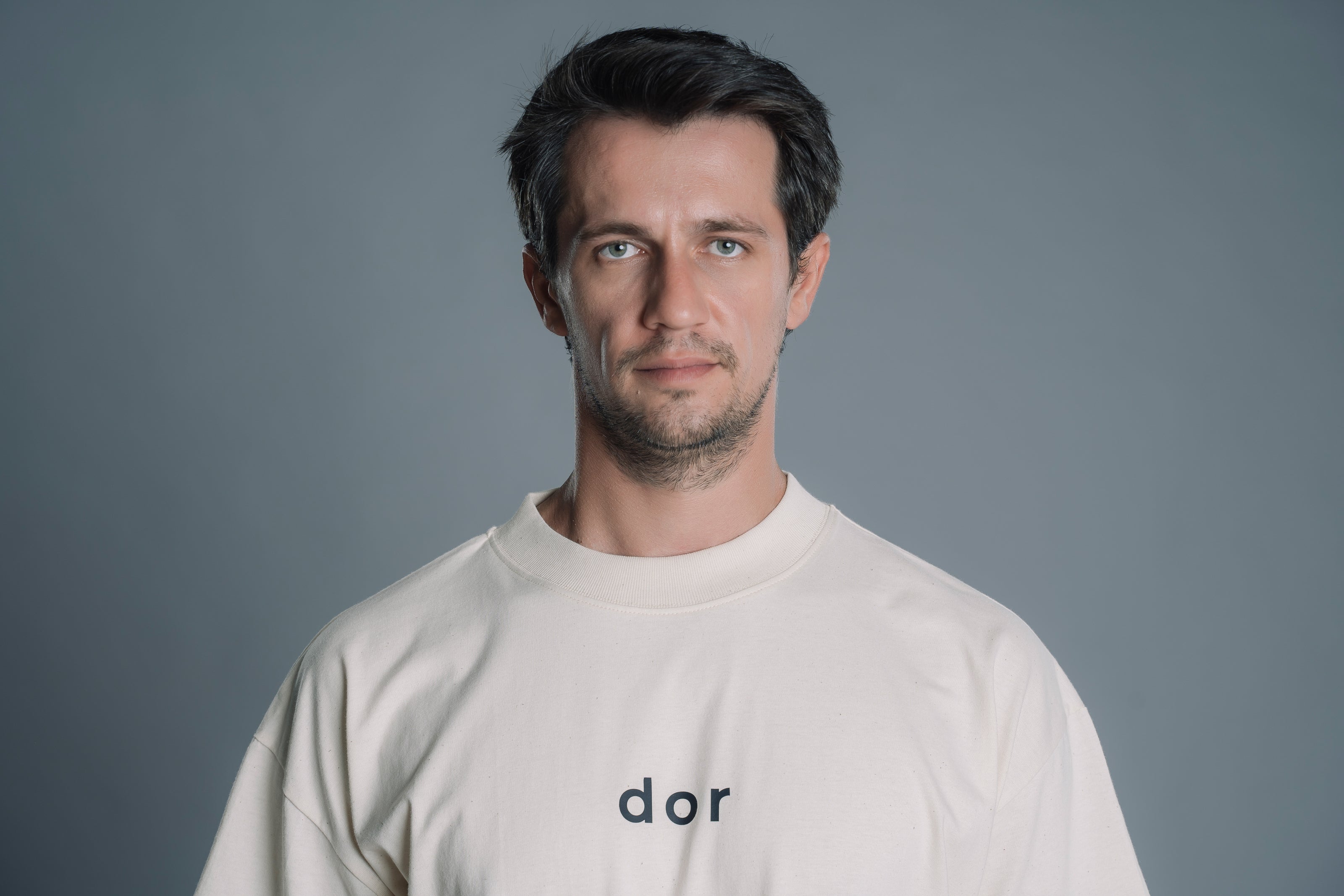 Man wearing a Natural RAW tshirt with 'dor' logo against a gray background